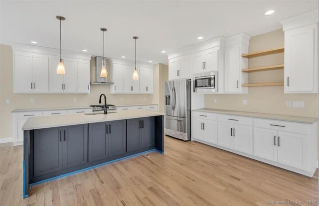 kitchen featuring wall chimney range hood, light wood-type flooring, light countertops, stainless steel appliances, and white cabinetry