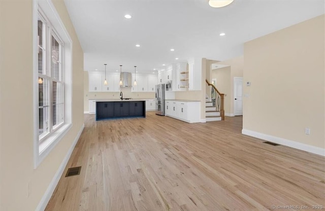 unfurnished living room featuring a sink, baseboards, light wood finished floors, and visible vents