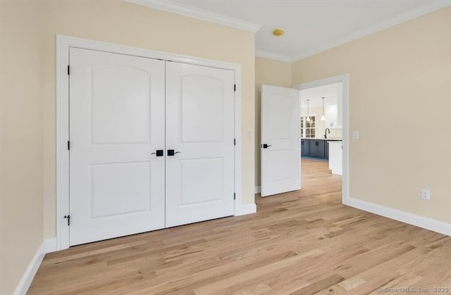 unfurnished bedroom featuring crown molding, a closet, baseboards, and light wood-style floors