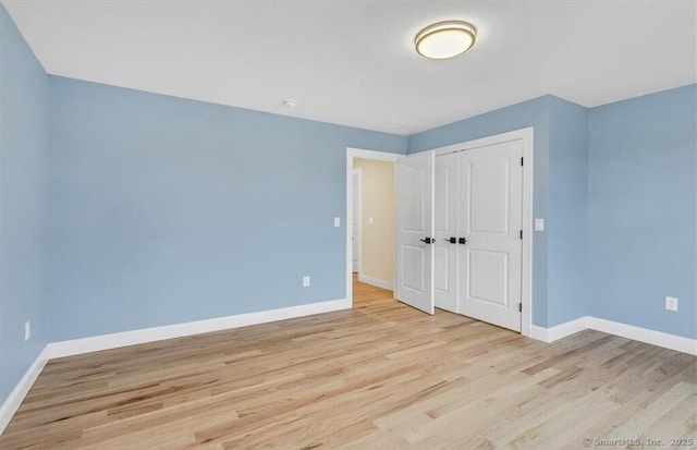 unfurnished bedroom featuring baseboards, light wood-style flooring, and a closet