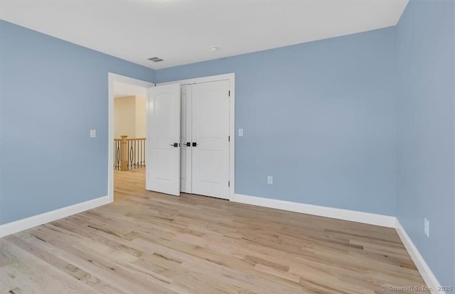 unfurnished bedroom featuring a closet, baseboards, visible vents, and light wood-type flooring