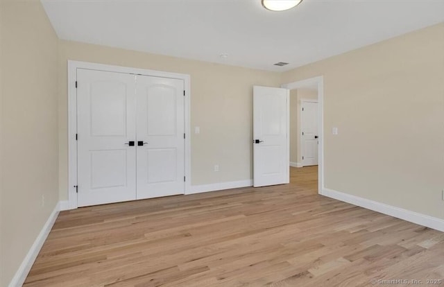 unfurnished bedroom featuring baseboards, light wood-style flooring, and a closet
