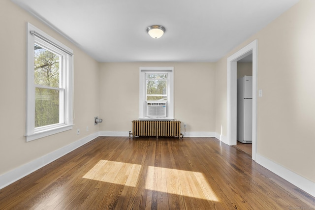 unfurnished room with baseboards, cooling unit, radiator heating unit, and hardwood / wood-style floors