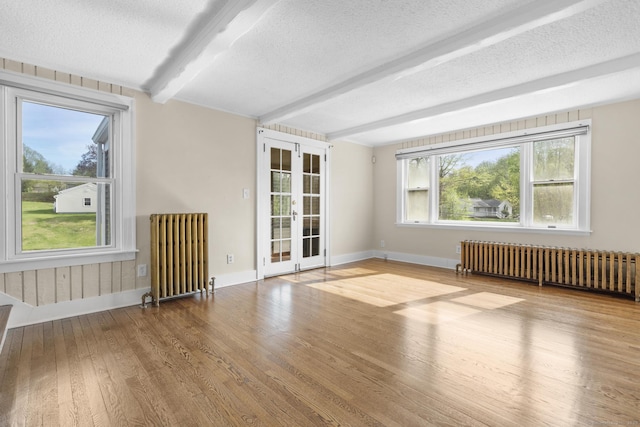 unfurnished room with radiator, beamed ceiling, a textured ceiling, and wood finished floors