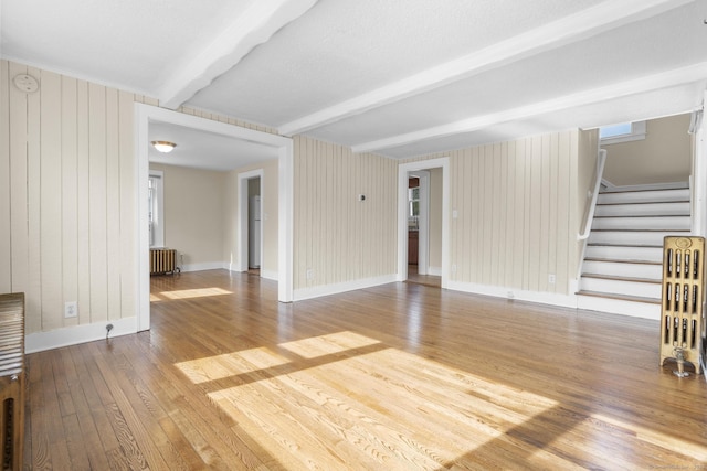 unfurnished living room with wood finished floors, stairway, baseboards, beamed ceiling, and radiator heating unit