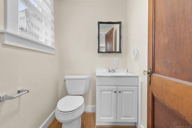 half bath with baseboards, wood finished floors, toilet, and vanity
