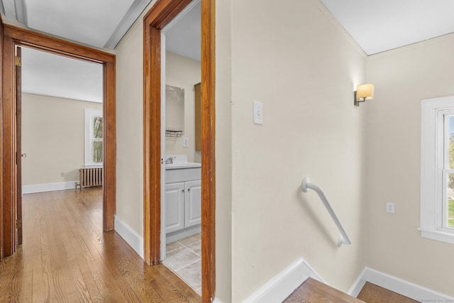 hallway featuring a sink, baseboards, an upstairs landing, light wood-style floors, and radiator