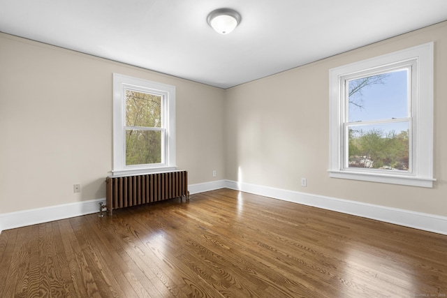 empty room featuring baseboards, a healthy amount of sunlight, radiator heating unit, and hardwood / wood-style floors