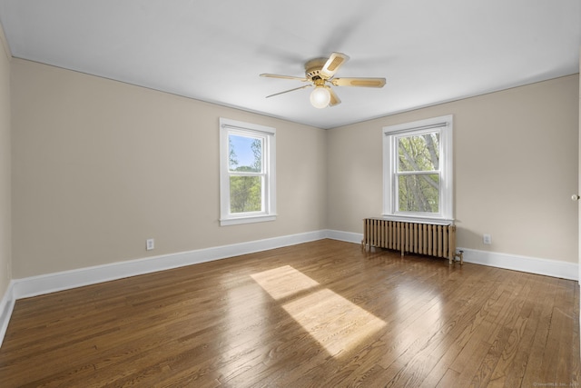 empty room with baseboards, a ceiling fan, radiator heating unit, and hardwood / wood-style flooring