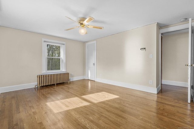 unfurnished room with wood finished floors, baseboards, ceiling fan, and radiator heating unit