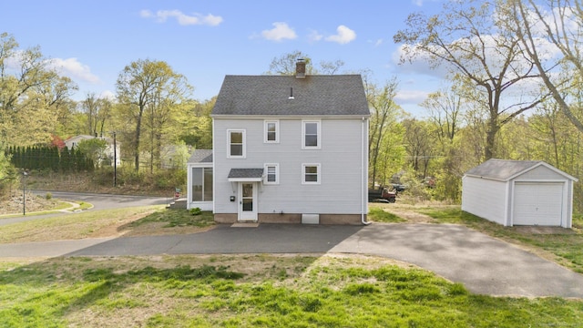 back of house with a shingled roof, a chimney, and an outdoor structure
