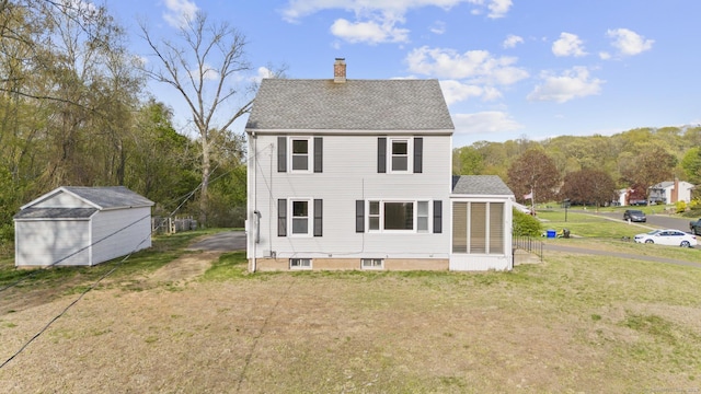 rear view of property featuring a shingled roof, a sunroom, a chimney, an outdoor structure, and a yard
