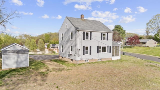 view of side of home featuring a storage unit, a shingled roof, an outbuilding, a chimney, and a yard