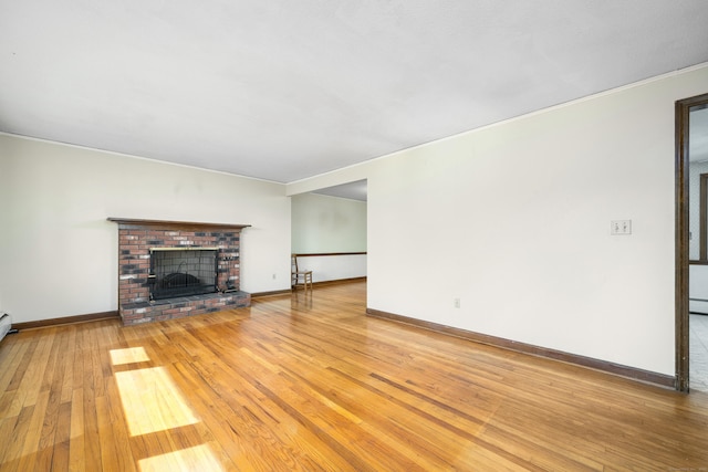 unfurnished living room with light wood-type flooring, ornamental molding, a brick fireplace, and baseboards