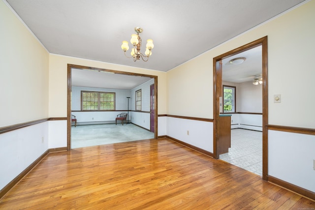 empty room with a chandelier, wood finished floors, plenty of natural light, baseboards, and crown molding