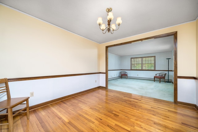 spare room with a chandelier, hardwood / wood-style floors, baseboards, and wallpapered walls