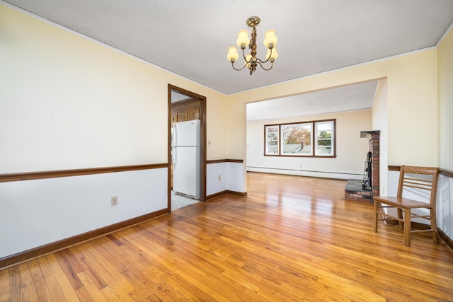spare room with a baseboard heating unit, a chandelier, light wood-type flooring, and baseboards