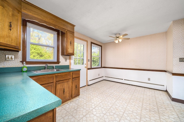 kitchen featuring wallpapered walls, a sink, a ceiling fan, brown cabinetry, and a baseboard heating unit