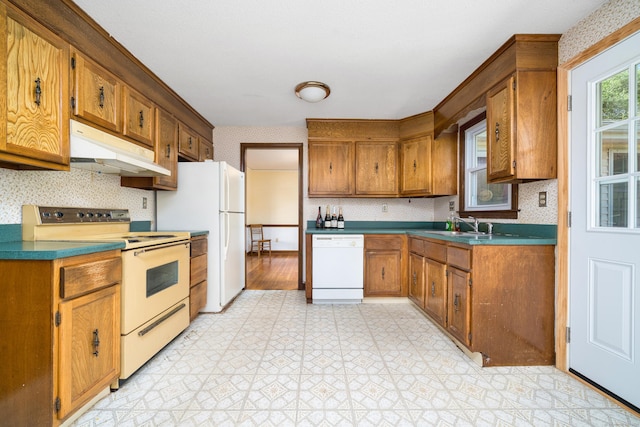 kitchen with under cabinet range hood, white appliances, light flooring, wallpapered walls, and brown cabinets