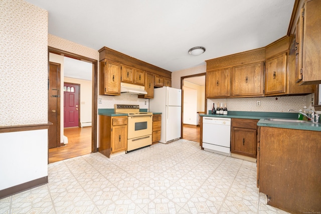 kitchen featuring white appliances, under cabinet range hood, wallpapered walls, a sink, and light flooring