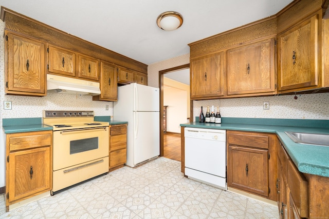 kitchen with white appliances, under cabinet range hood, wallpapered walls, and brown cabinetry