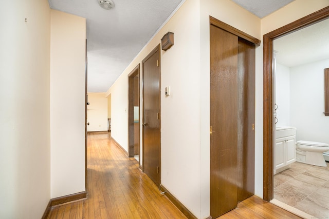 corridor featuring light wood-type flooring and baseboards