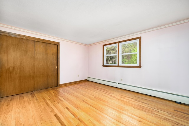 unfurnished bedroom with light wood-style flooring, baseboard heating, a closet, baseboards, and ornamental molding