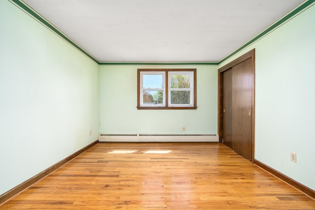 unfurnished bedroom with baseboard heating, ornamental molding, light wood finished floors, and baseboards