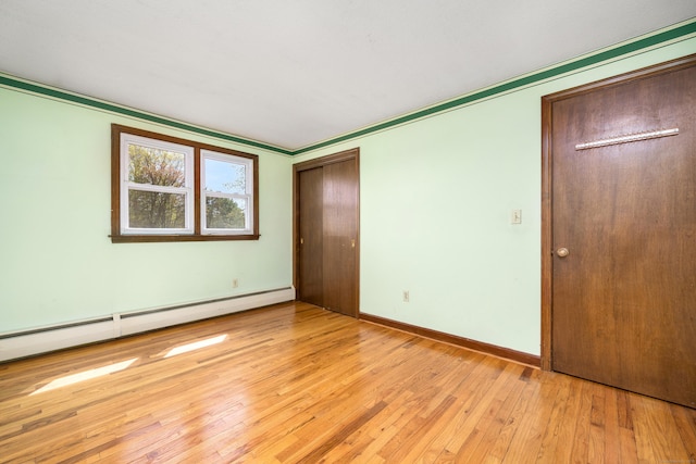 unfurnished bedroom with baseboard heating, light wood-type flooring, and baseboards