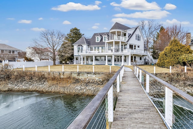 view of dock with a lawn, fence, a water view, and a balcony