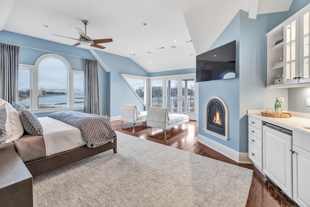 bedroom with vaulted ceiling, a glass covered fireplace, dark wood finished floors, and multiple windows