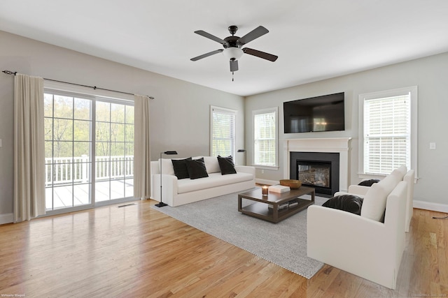 living area with baseboards, a ceiling fan, light wood-style flooring, and a glass covered fireplace
