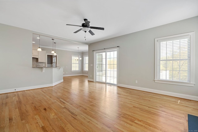 unfurnished living room with a sink, baseboards, ceiling fan with notable chandelier, and light wood-type flooring