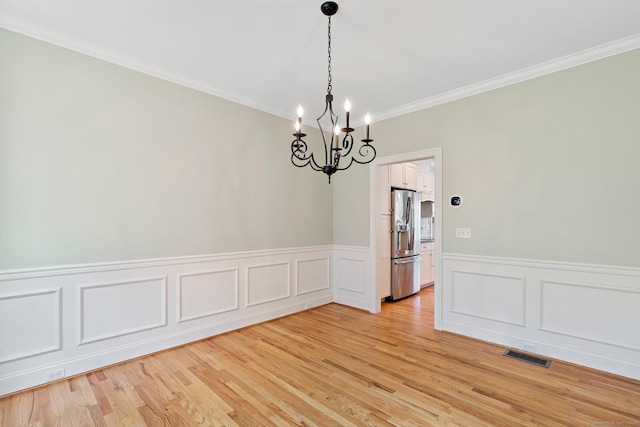 empty room featuring visible vents, a wainscoted wall, an inviting chandelier, ornamental molding, and light wood-style flooring