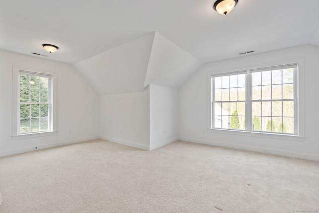 additional living space with visible vents, baseboards, vaulted ceiling, and light colored carpet