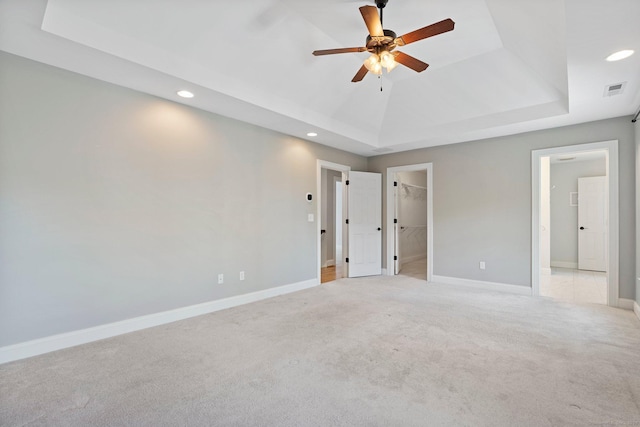unfurnished bedroom with recessed lighting, a tray ceiling, and light carpet