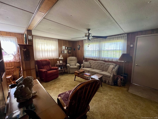 carpeted living area with wooden walls, a ceiling fan, and a textured ceiling