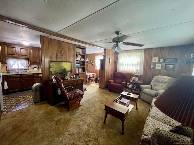 living room featuring wooden walls, carpet floors, a ceiling fan, and a textured ceiling