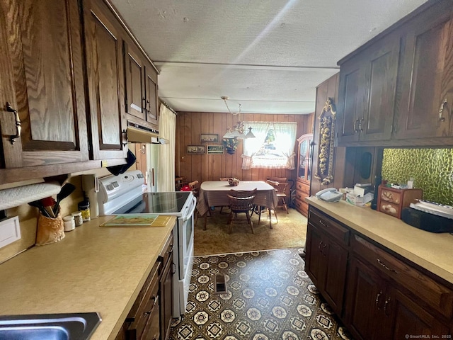 kitchen with light countertops, under cabinet range hood, wooden walls, and white range with electric cooktop