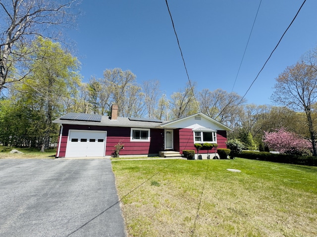 single story home with aphalt driveway, a chimney, a garage, roof mounted solar panels, and a front lawn