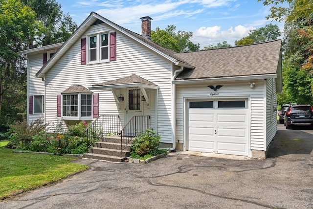 view of front facade featuring an attached garage, a chimney, a shingled roof, and aphalt driveway