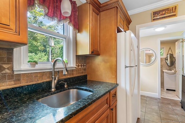 kitchen with light tile patterned flooring, a sink, brown cabinetry, freestanding refrigerator, and dark stone counters
