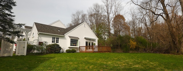 rear view of house featuring a deck, a yard, and roof with shingles
