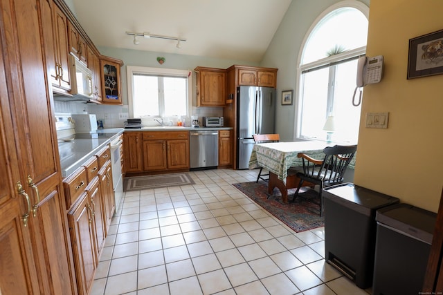 kitchen featuring stainless steel appliances, brown cabinets, backsplash, vaulted ceiling, and track lighting