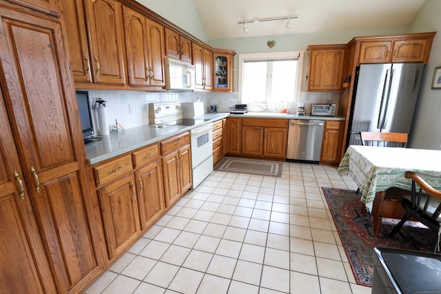 kitchen featuring stainless steel appliances, backsplash, lofted ceiling, brown cabinetry, and light tile patterned floors