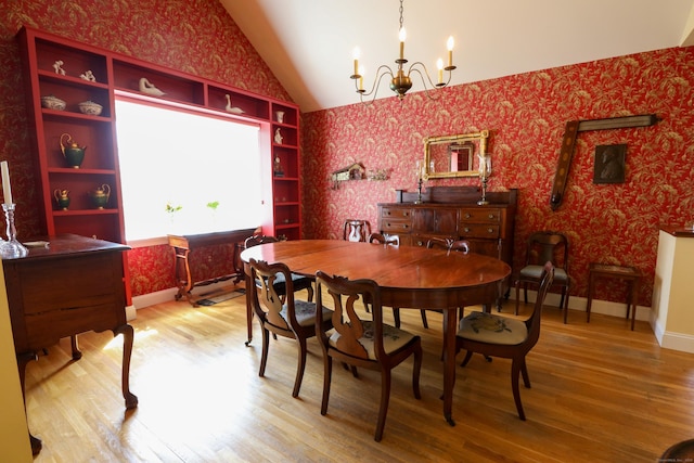 dining space featuring wallpapered walls, lofted ceiling, a chandelier, wood finished floors, and baseboards
