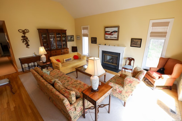 living area with wood finished floors, lofted ceiling, and a fireplace with flush hearth