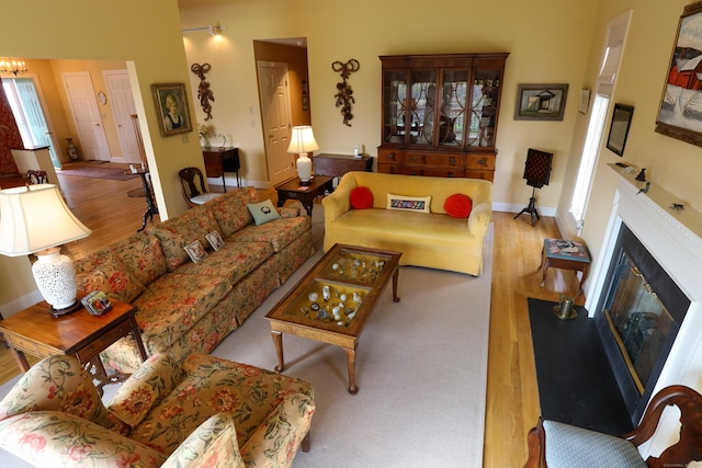 living area with wood finished floors, baseboards, a glass covered fireplace, and a chandelier