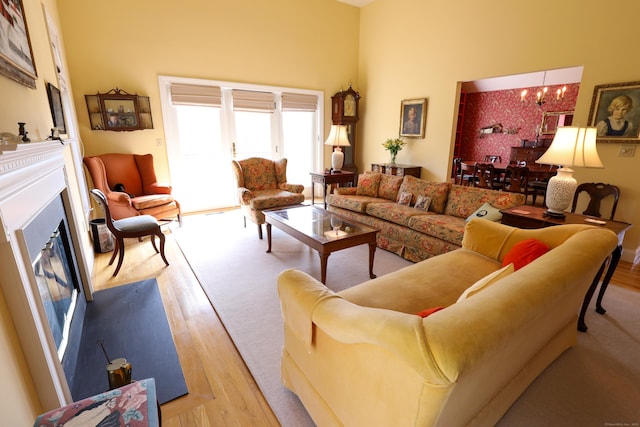 living area featuring a fireplace with flush hearth, wood finished floors, a chandelier, and a high ceiling