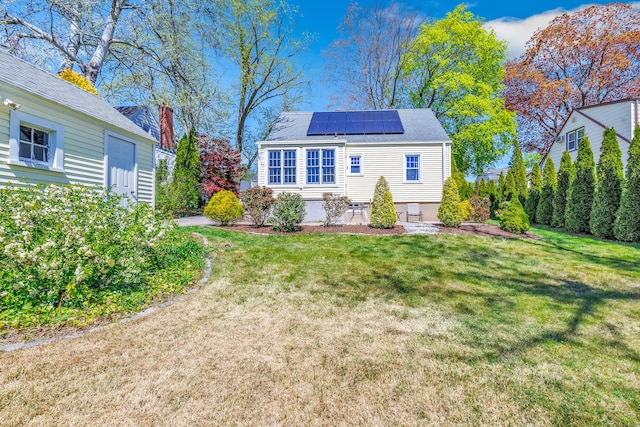rear view of house featuring a shingled roof, a yard, and solar panels